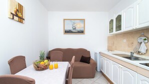 A compact kitchen with white cabinets, a dining area with a table and chairs, and a brown sofa. - Apartment Ivan Vrsi (Vrsi)