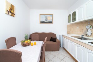 Eine kompakte Küche mit weißen Schränken, ein Essbereich mit Tisch und Stühlen sowie ein braunes Sofa.