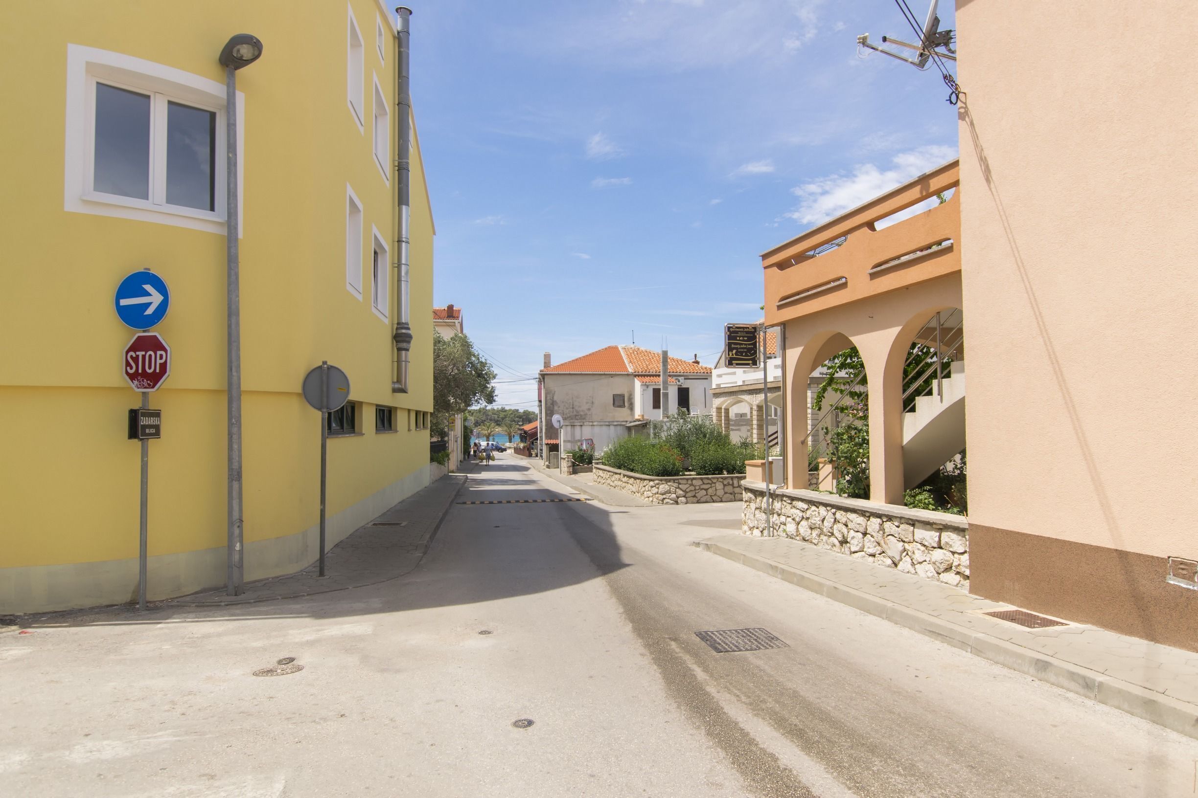 Une rue étroite, bordée de bâtiments des deux côtés, avec un panneau de signalisation indiquant un arrêt et un panneau de direction.