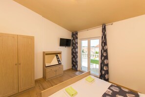 Une chambre à coucher comprenant un lit, une armoire en bois, un téléviseur et une porte-fenêtre coulissante donnant sur un espace extérieur.