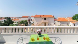 A balcony with a table set for two, a vase with flowers, and a view of buildings with orange roofs. - Apartments and Room Central Position (Novalja)