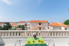 A balcony with a table set for two, a vase with flowers, and a view of buildings with orange roofs.