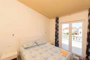 Une chambre à coucher avec un lit, une table de chevet, une fenêtre avec des rideaux et une vue sur les bâtiments à l’extérieur.