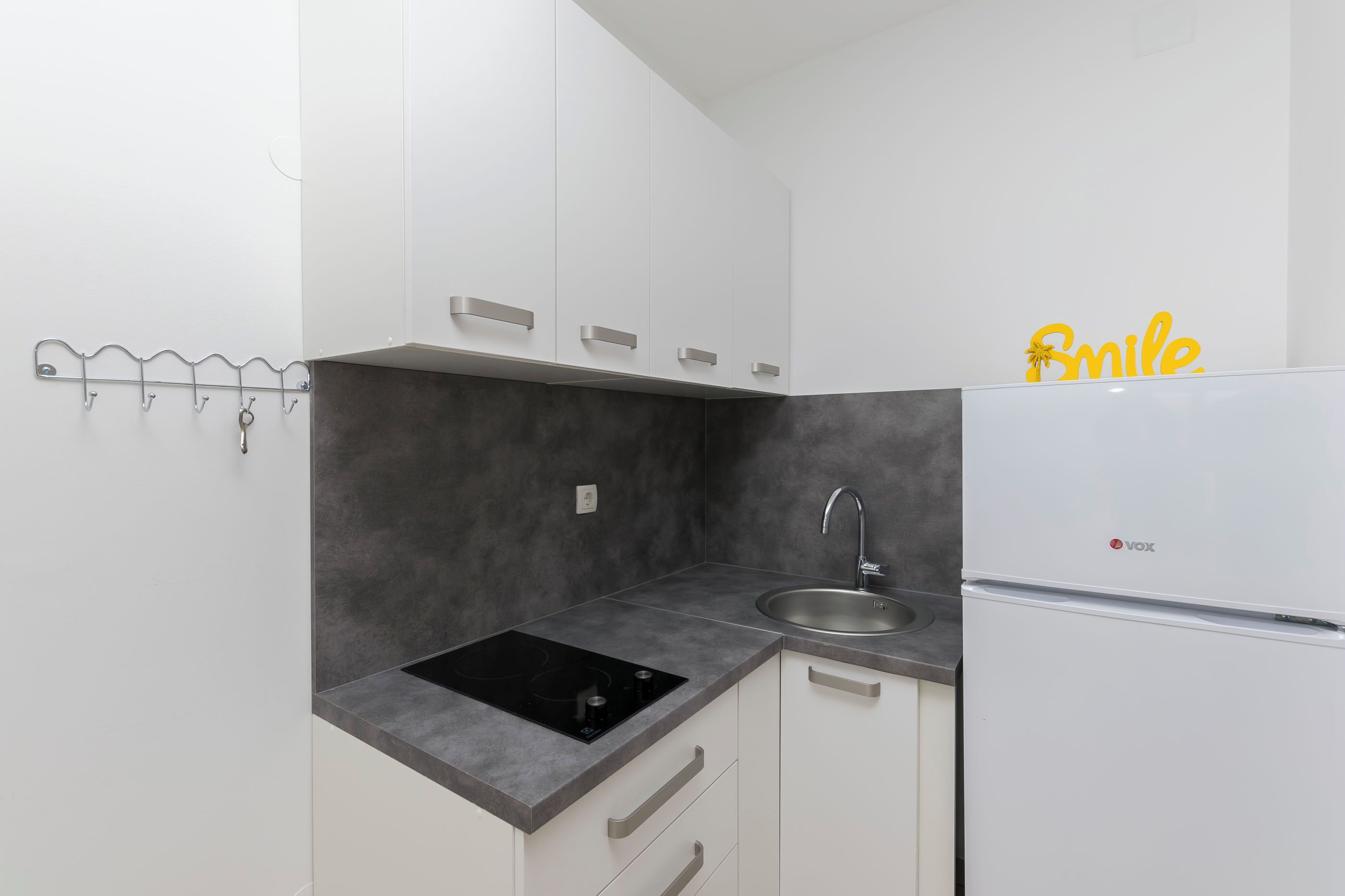A kitchen with white cabinets, a black countertop, a sink, and a white refrigerator.