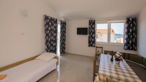 A room with a bed, a dining table with chairs, a TV mounted on the wall, and a window with curtains. - Apartments and Room Central Position (Novalja)