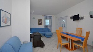 A living room with a blue sofa, a dining table with chairs, and a television mounted on the wall. - Apartments Mira (Starigrad - Paklenica)
