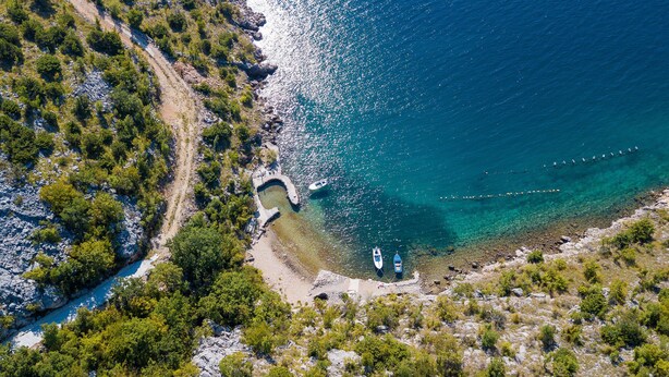 An aerial view of a coastal area with rocky terrain, clear turquoise waters, and a few boats. - Apartments Mira (Starigrad - Paklenica)
