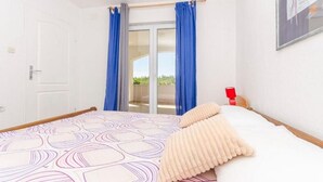 A hotel room with a bed, a window with blue curtains, a door, and a red lamp on the nightstand. - Apartments Mira (Starigrad - Paklenica)