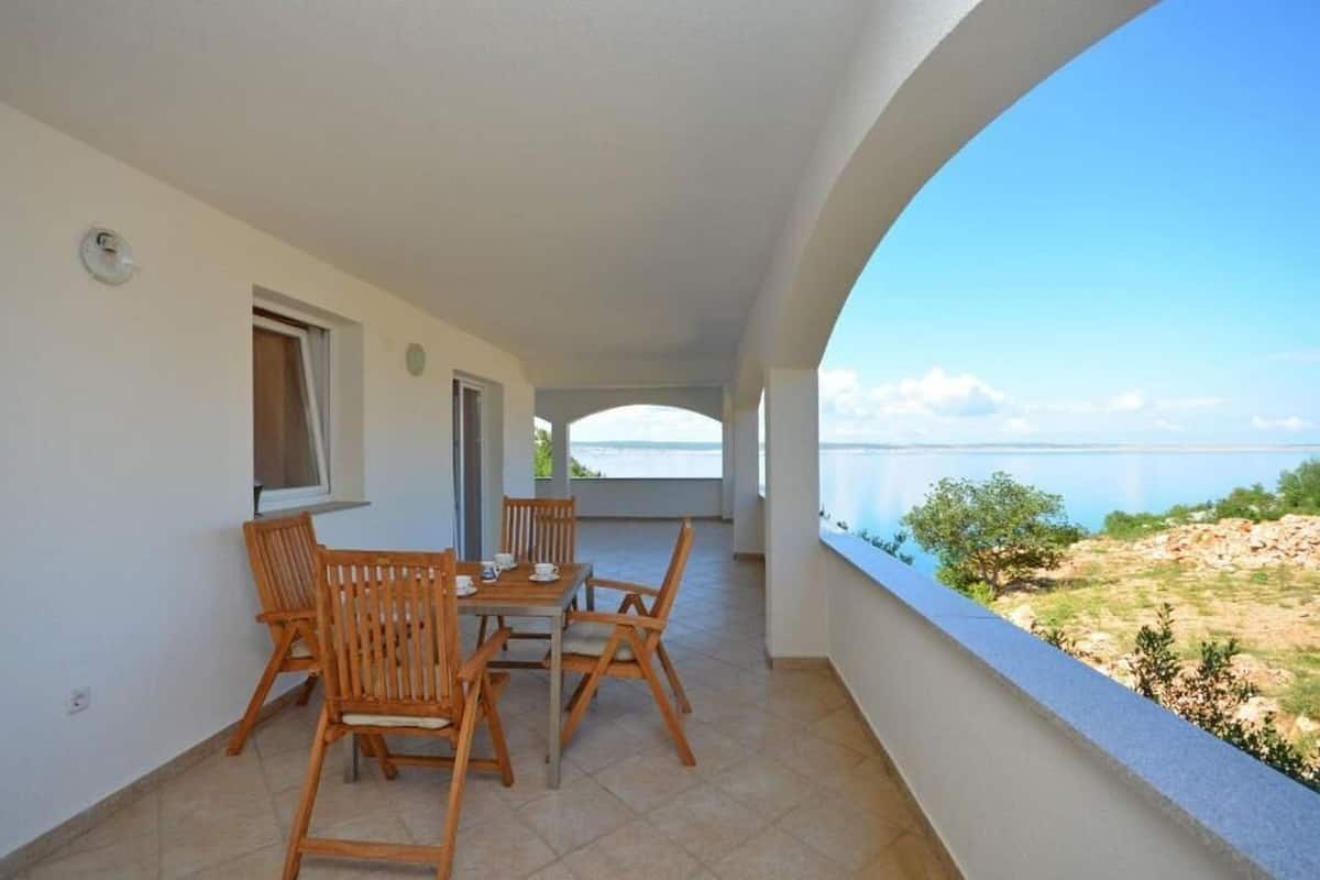 Un balcón con mesa y sillas, vista al mar y cielo despejado.