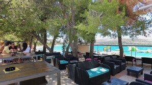 An outdoor seating area with wicker furniture and tables, overlooking a beach and the sea. - Apartments Villa Niko (Arbanija)