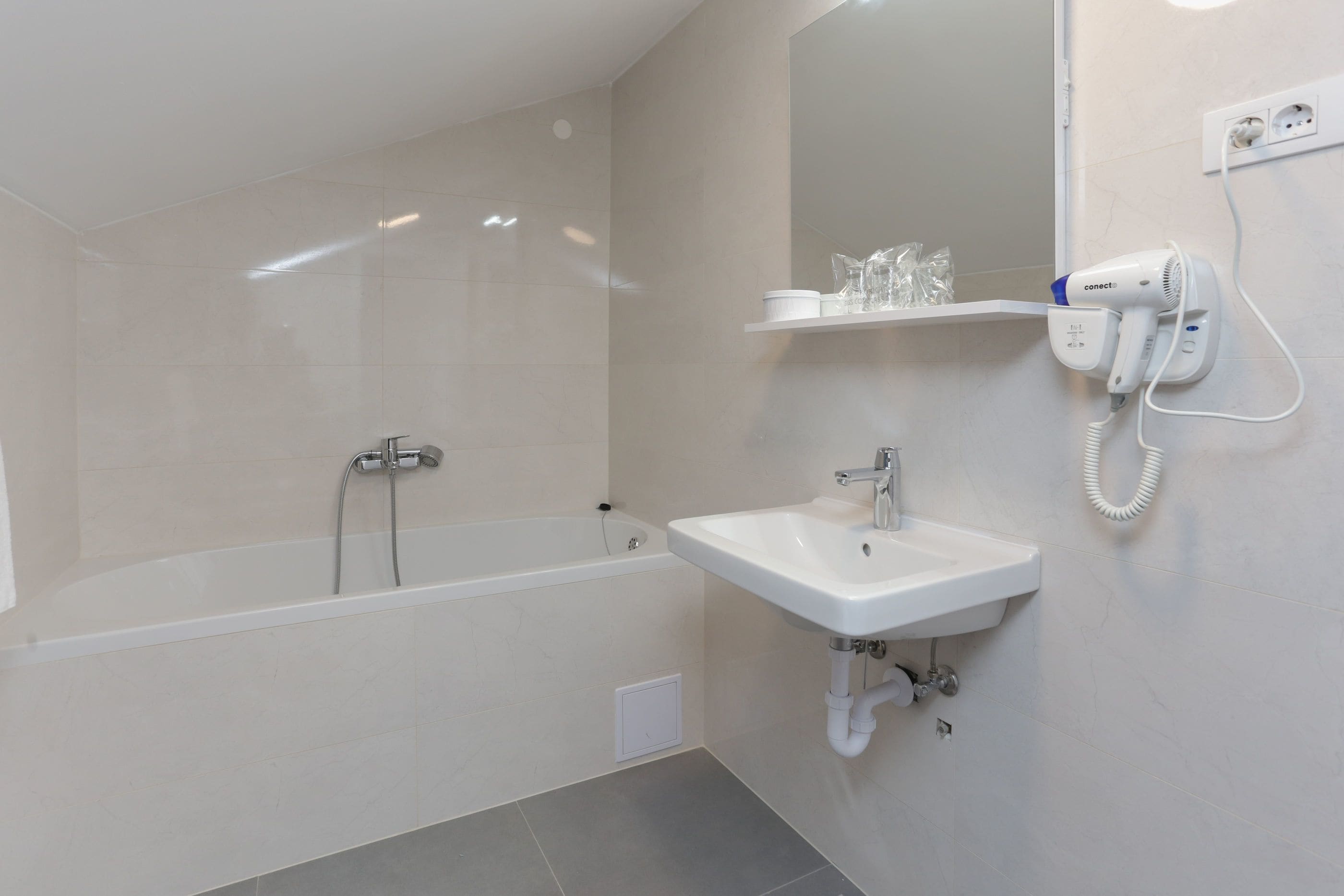 A modern bathroom with a bathtub, a sink, and a hairdryer mounted on the wall.