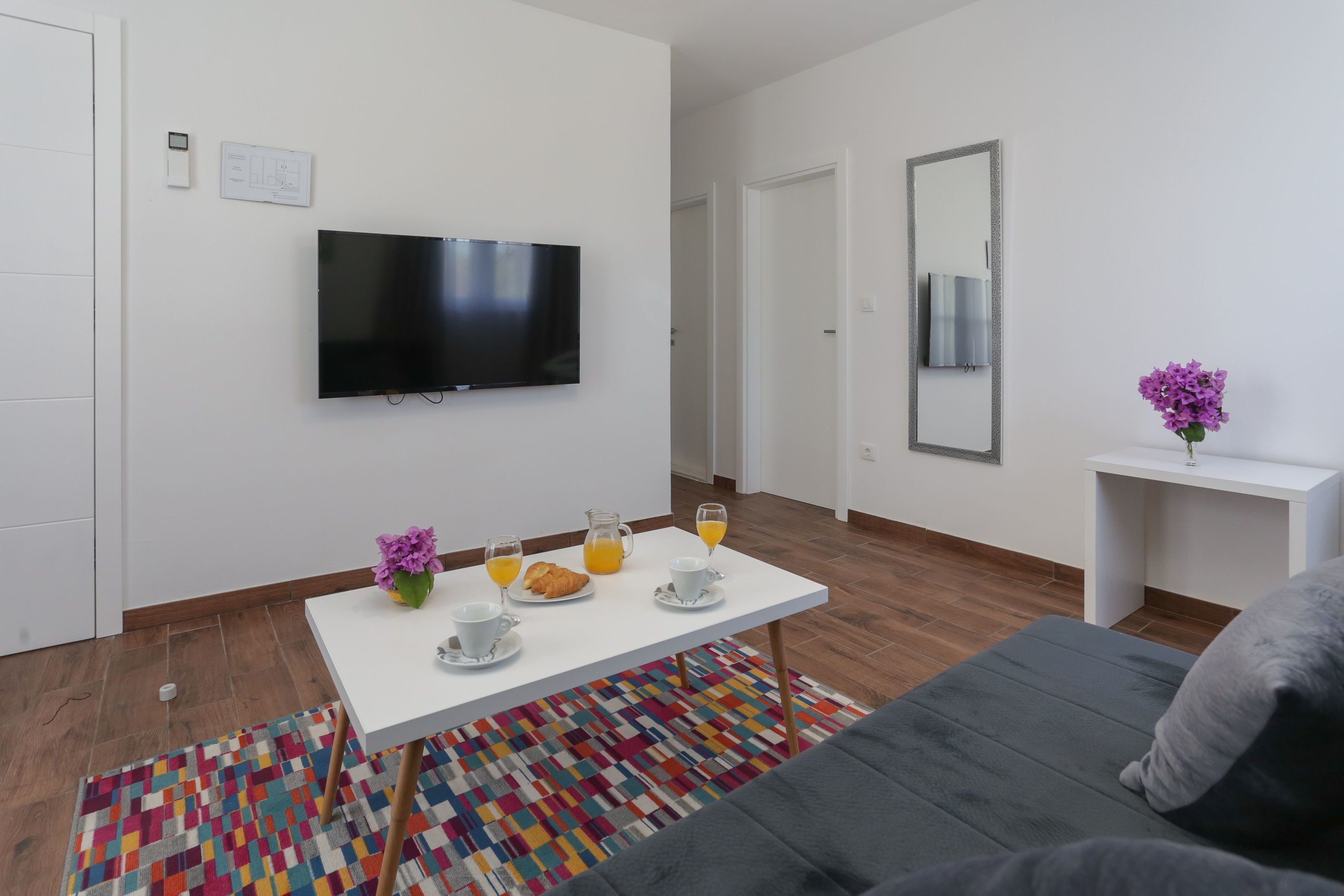 A modern living room with a flat-screen TV, a dining table with breakfast items, a sofa, and a mirror.