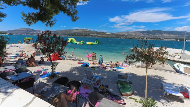 A beach with sun loungers, umbrellas, and a clear view of the sea and mountains. - Apartments Villa Niko (Arbanija)
