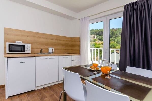Una cocina moderna con microondas, cafetera y armarios blancos. Hay una mesa de comedor con sillas y vistas a un balcón con cortinas.