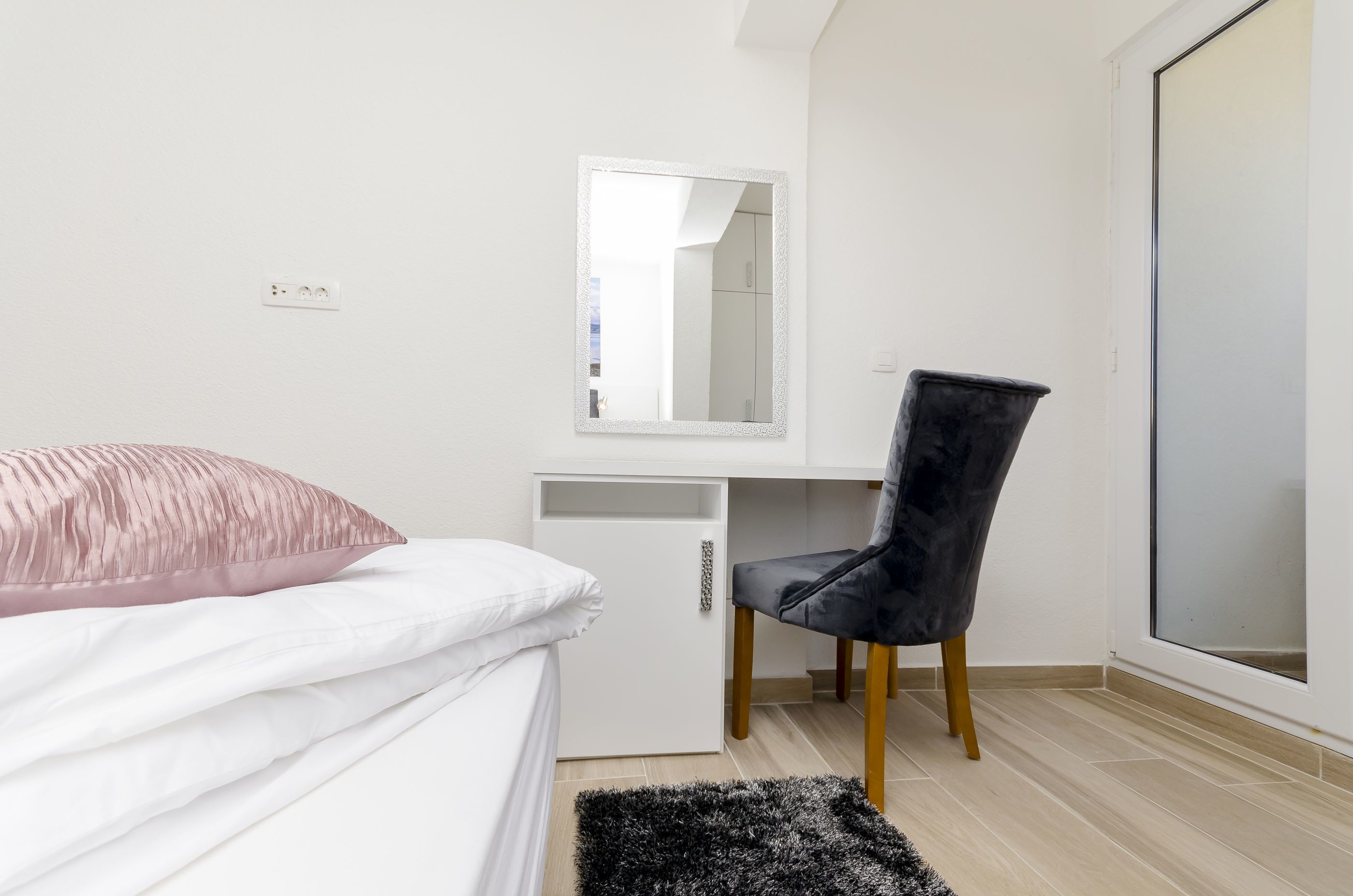 A bedroom with a bed, a desk with a chair, a mirror, and a window.