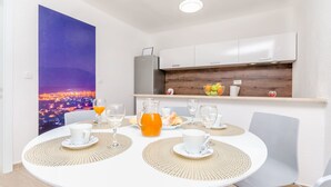 A dining area with a round table set for two, a pitcher of orange juice, and a breakfast spread. - Apartments Villa Niko (Arbanija)