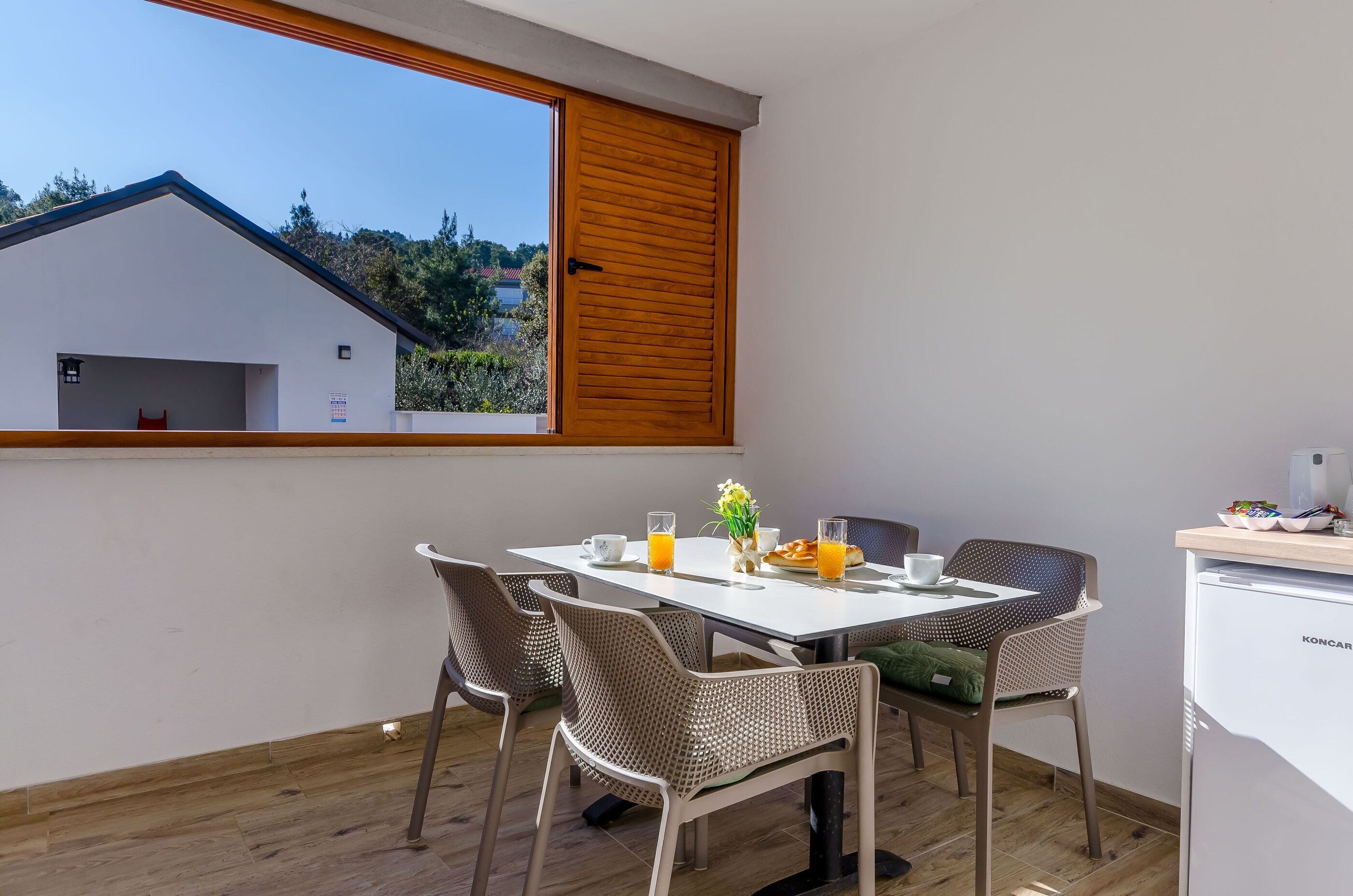 Ein Essbereich mit Tisch, Stühlen und Blick auf ein Gebäude durch ein Fenster.