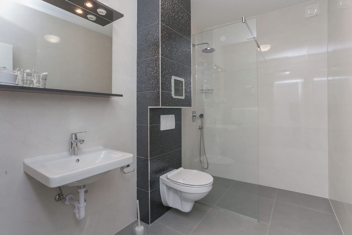 Een moderne badkamer met een wit wastafelmeubel, toilet en een douche met glazen wanden.