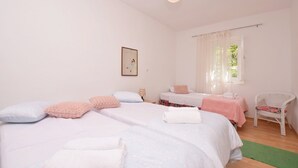 A room with two beds, a chair, a window with curtains, and a hanging light fixture. - House Green Paradise (Vrpolje)
