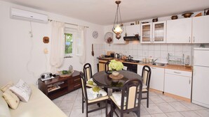 A compact kitchen with white cabinets, a dining table with chairs, and a hanging light fixture. - House Green Paradise (Vrpolje)
