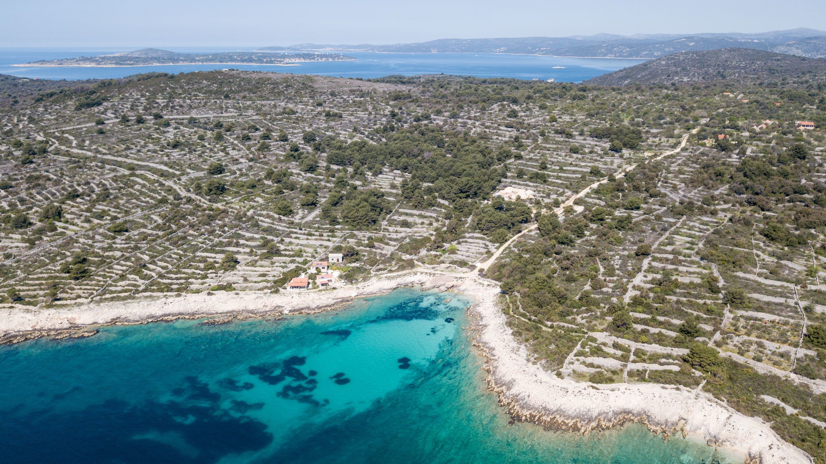 En vy över en kuststad sedd från luften, med terrasserade åkrar, en strand och ett klart, blått hav.