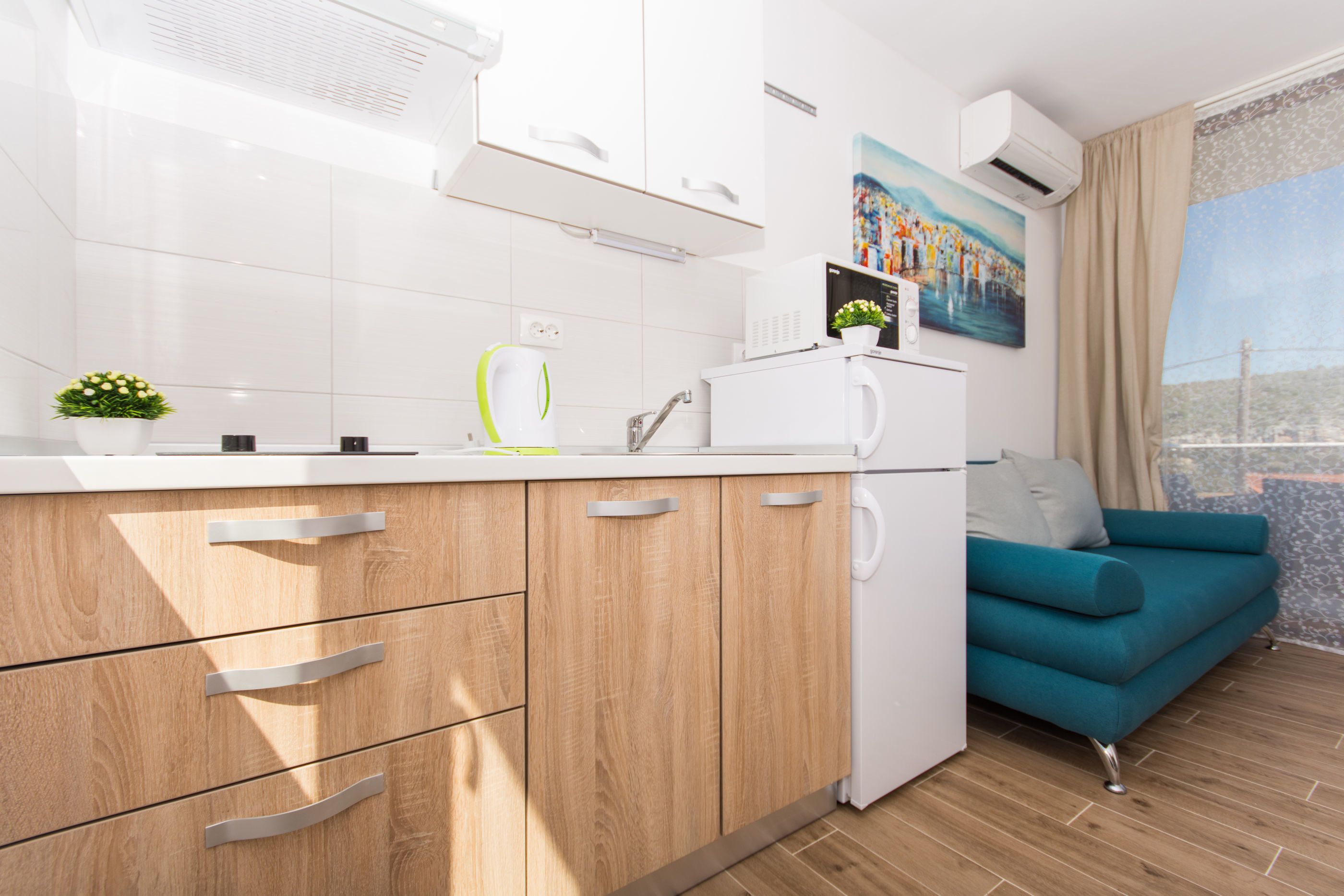 A modern kitchen with wooden cabinets, a white countertop, and a teal sofa.
