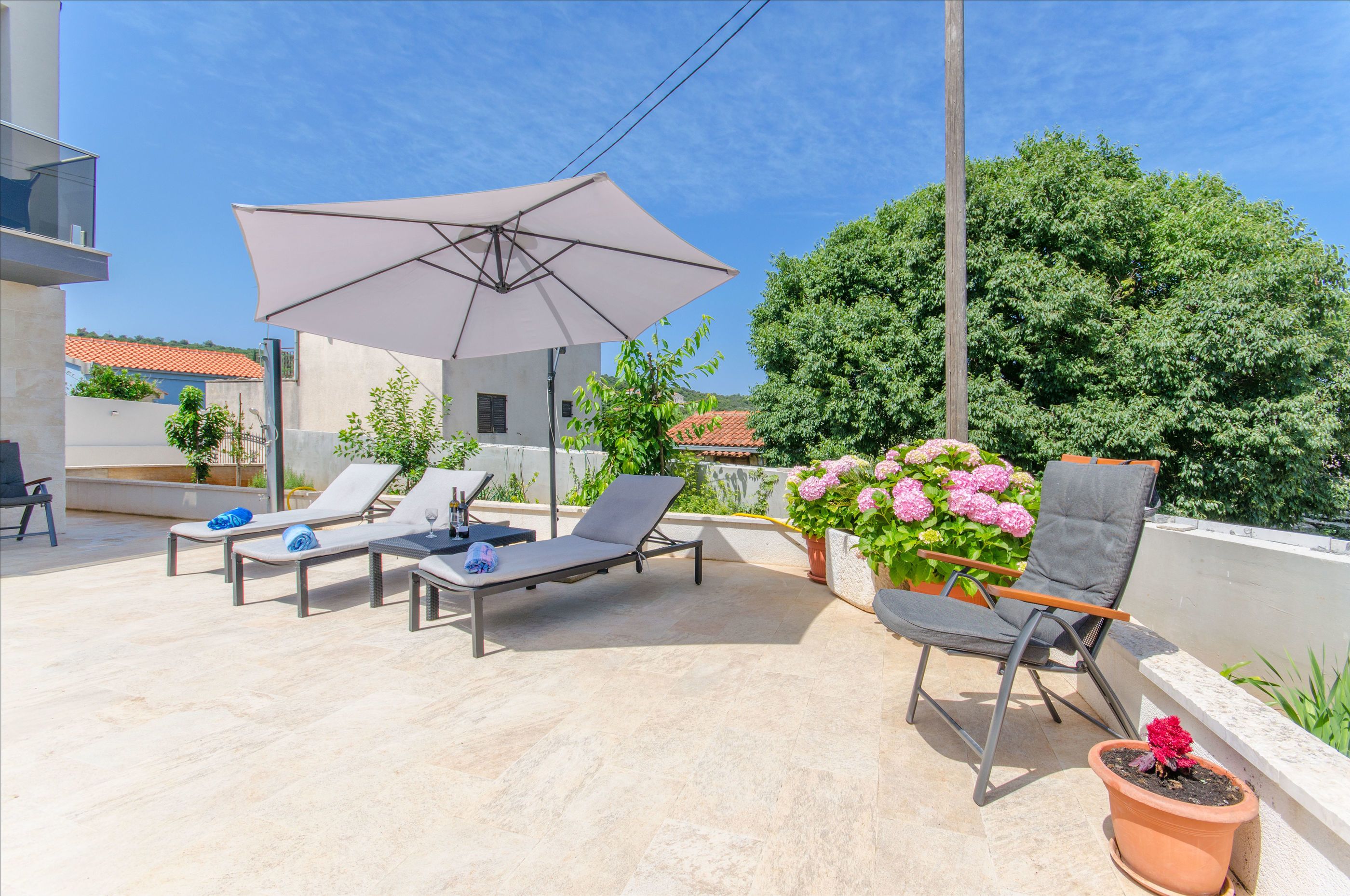 A rooftop terrace with lounge chairs, a large umbrella, and potted plants.