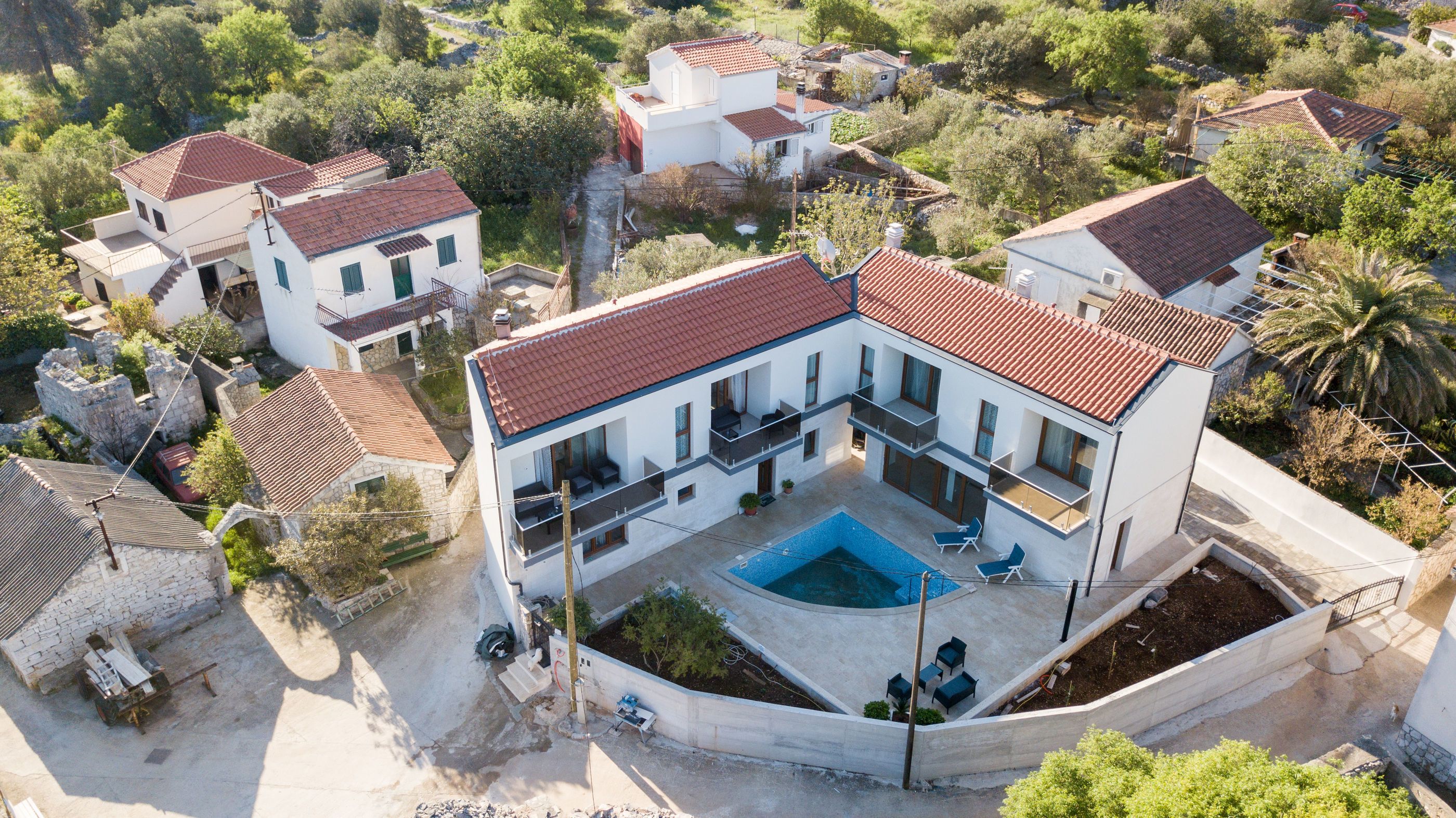 A two-story house with a swimming pool, surrounded by trees and other houses.