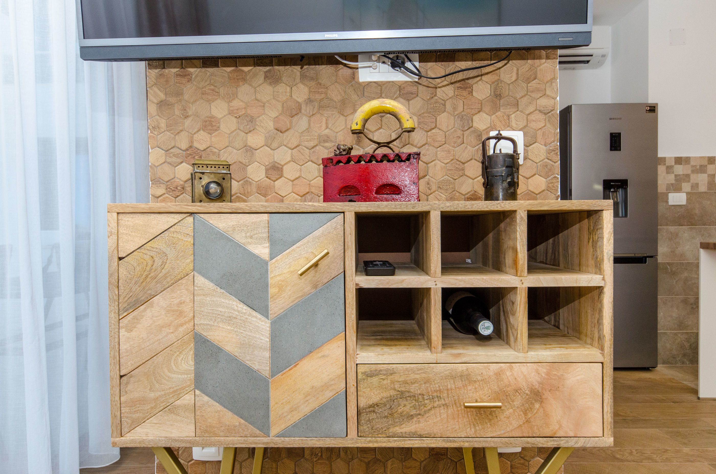 A kitchen with a wooden cabinet featuring geometric patterns, a stainless steel refrigerator, and a wall-mounted television.