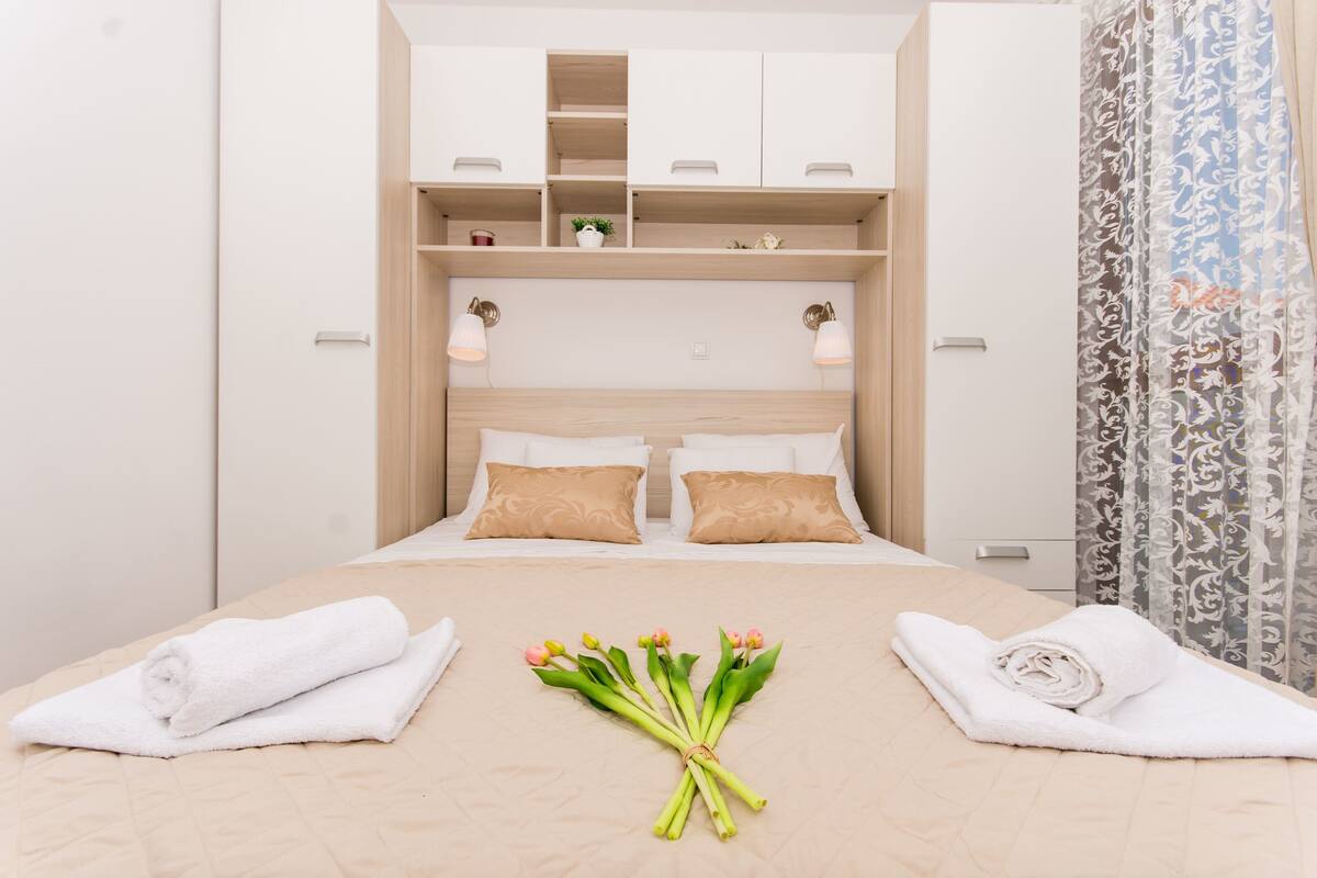A neatly made bed with white linens, a bouquet of flowers, and towels on either side.