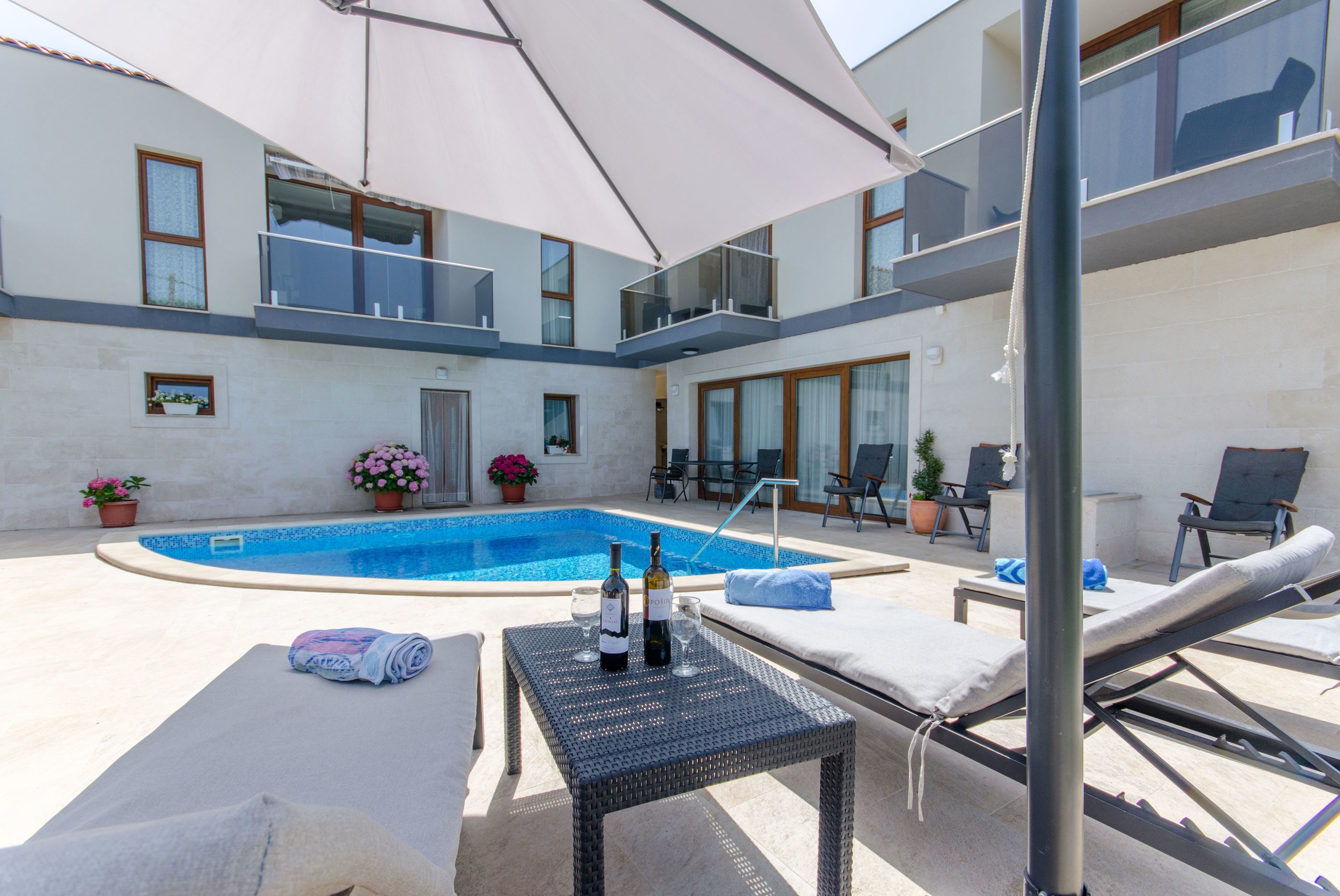 Un área junto a la piscina con sillones de descanso, una mesa con una botella y un vaso, y plantas en macetas.