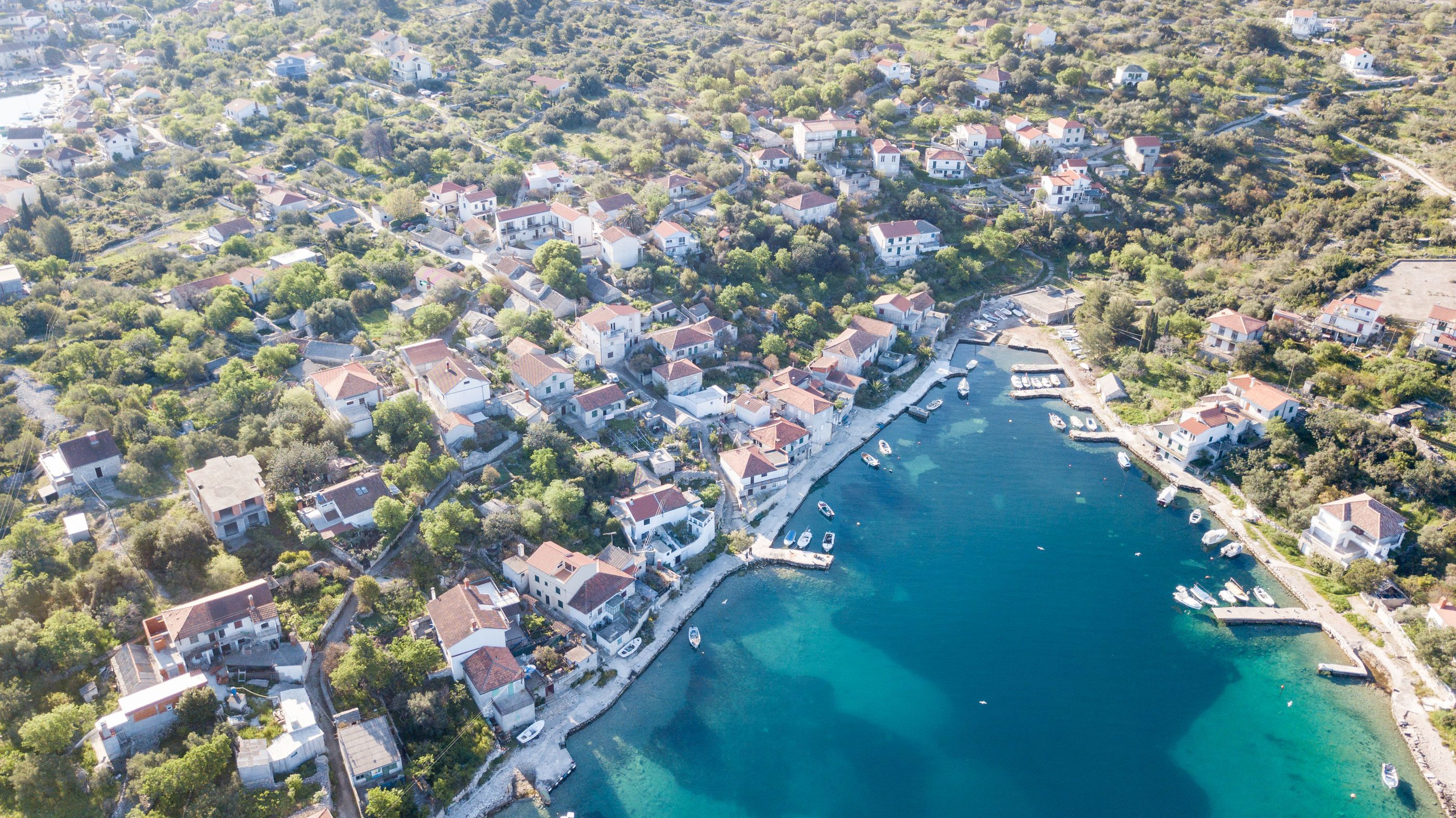 An aerial view of a coastal town with houses, a marina, and clear blue waters.