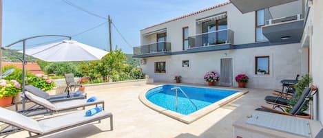 Un bâtiment moderne à deux étages, doté d’une piscine, d’un espace extérieur aménagé et de plantes en pot.