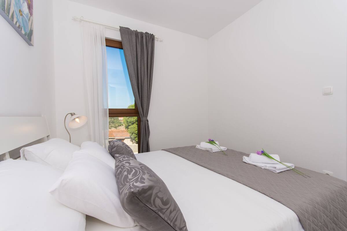 A hotel room with a large bed, a bedside table with a lamp, a window with curtains, and a view of the outdoors.
