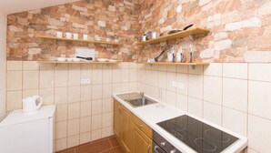 Une cuisine avec un mur de pierre derrière l’évier, des étagères en bois, une cuisinière et un évier.
