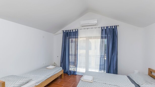 Une petite pièce lumineuse, avec deux lits simples, une fenêtre ornée de rideaux bleus et un climatiseur fixé au mur.