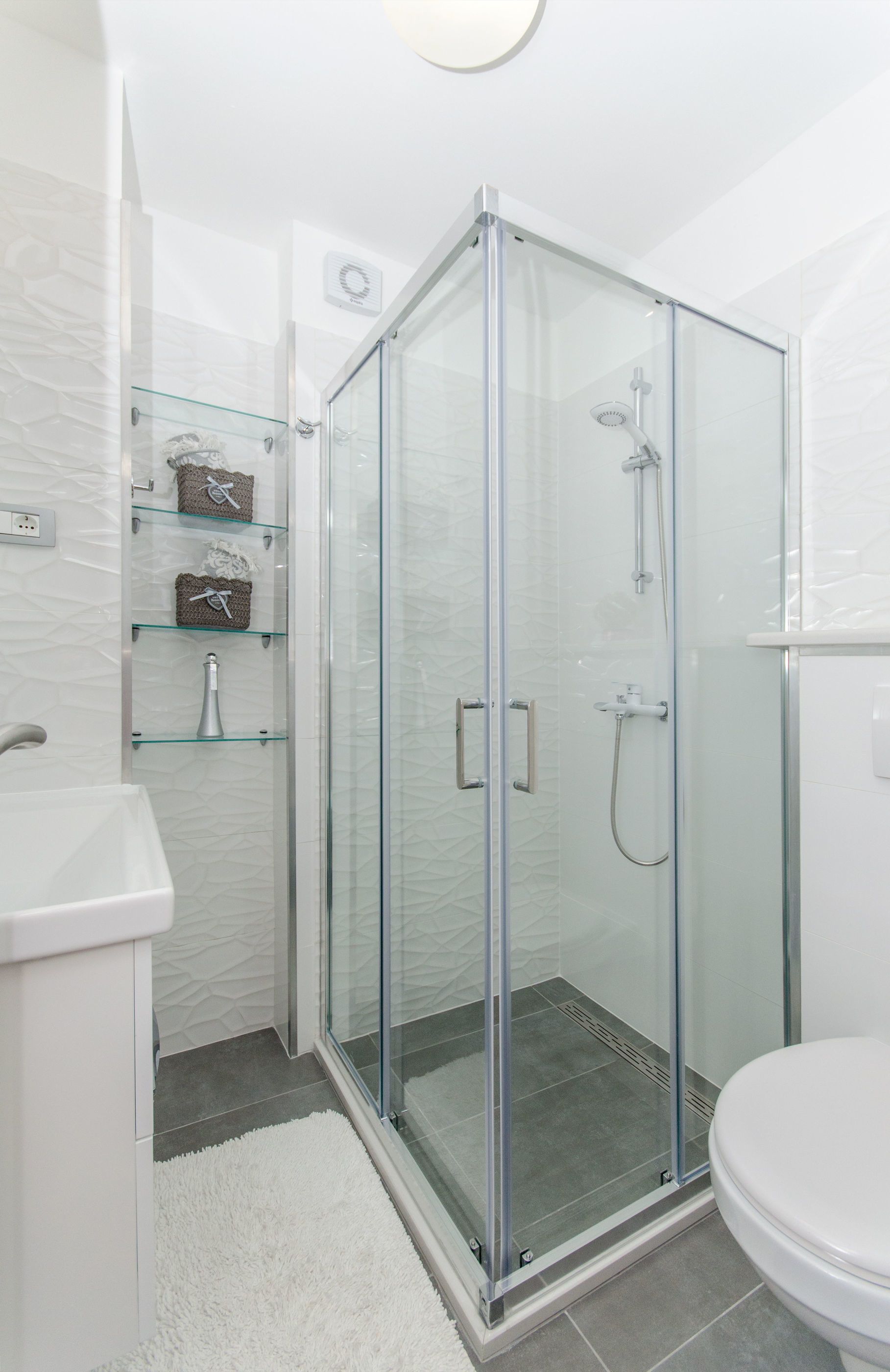 A modern bathroom with a glass-enclosed shower, a white sink, and a toilet.