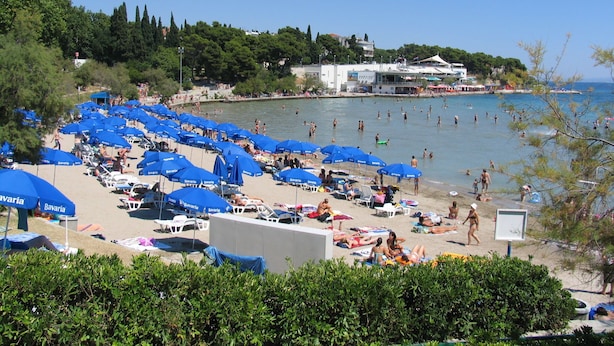 Una playa con numerosos sombrillas azules y gente nadando en el agua.