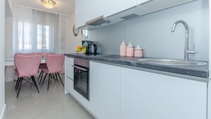 Una cocina moderna con armarios blancos, un lavamanos de acero inoxidable y una zona de comedor con sillas rosadas.