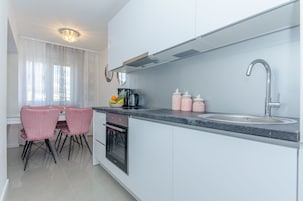 Une cuisine moderne avec des meubles blancs, un évier en acier inoxydable et un coin repas agrémenté de chaises roses.