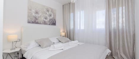 A modern bedroom with a large bed, a bedside table, a lamp, and a painting on the wall.