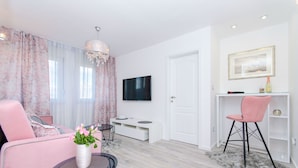 Una sala moderna con un sofá rosa, una mesa de centro redonda, un televisor montado en la pared y una pequeña mesita auxiliar blanca.