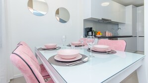 Un área de comedor moderna con una mesa de vidrio, sillas rosas y una cocina al fondo.