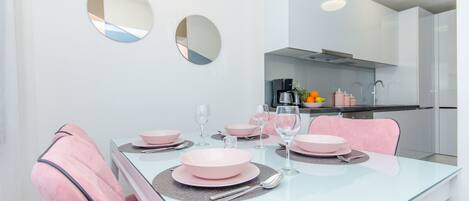 Un espace repas moderne avec une table en verre, des chaises roses et une cuisine en arrière-plan.