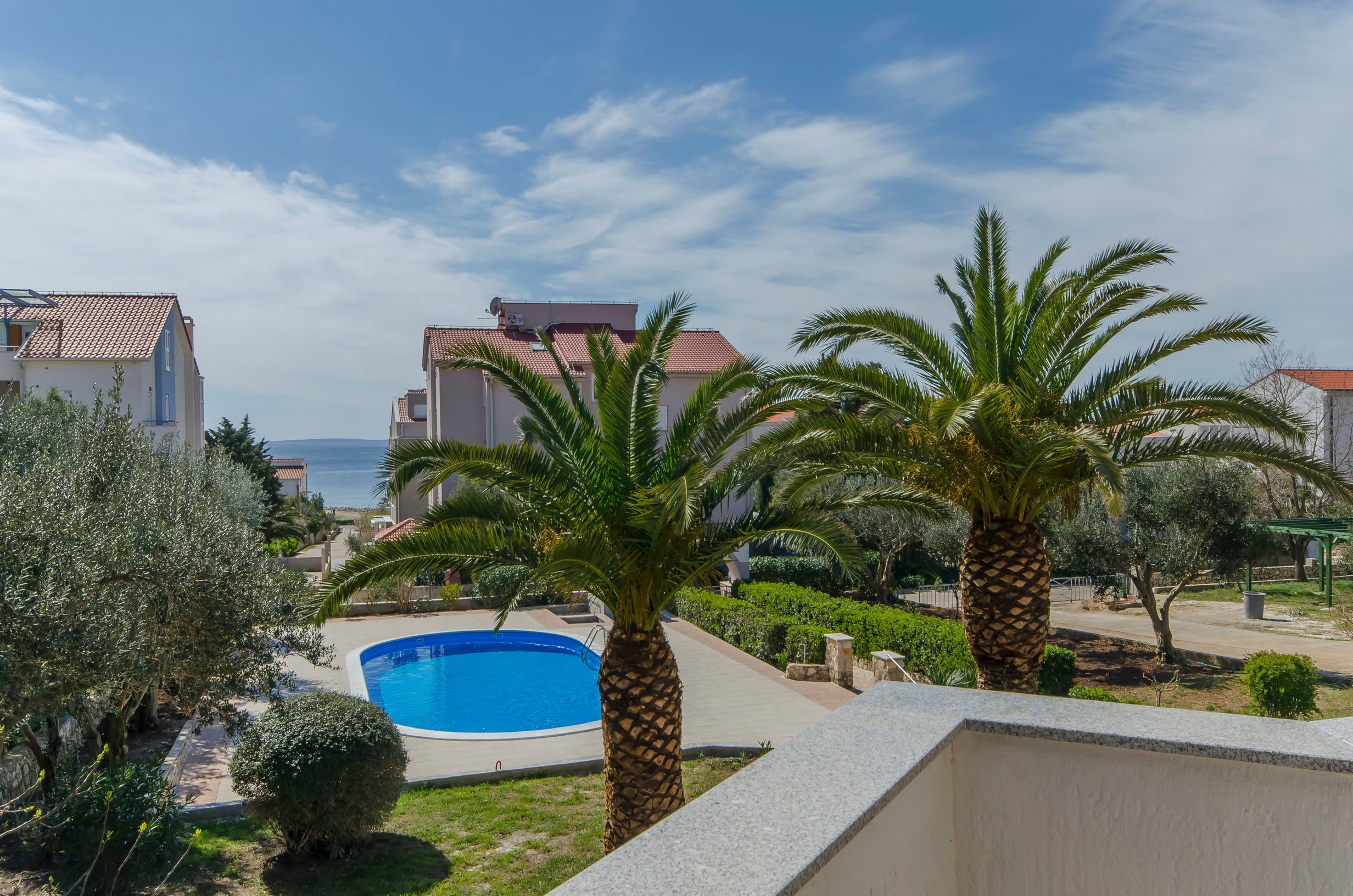 A residential area with a swimming pool, palm trees, and buildings with red-tiled roofs.