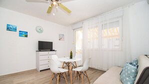 A bright, modern room with a dining table and chairs, a sofa, a TV, and a ceiling fan. - Apartments Tiho (Vodice)