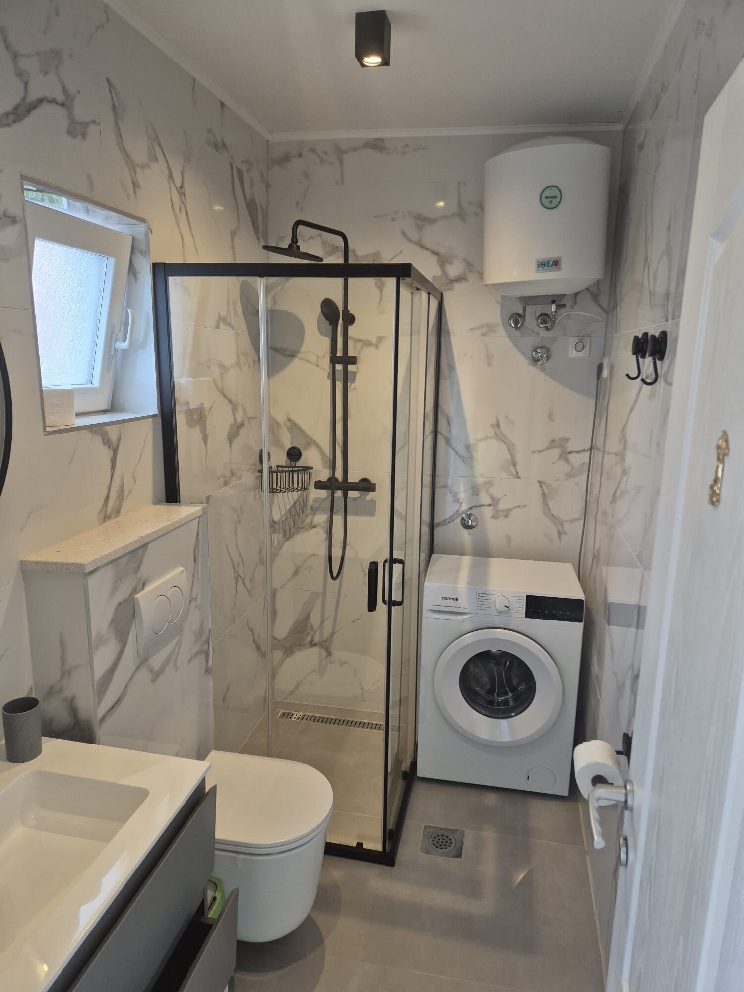 A compact bathroom with a glass shower enclosure, a washing machine, and a toilet.