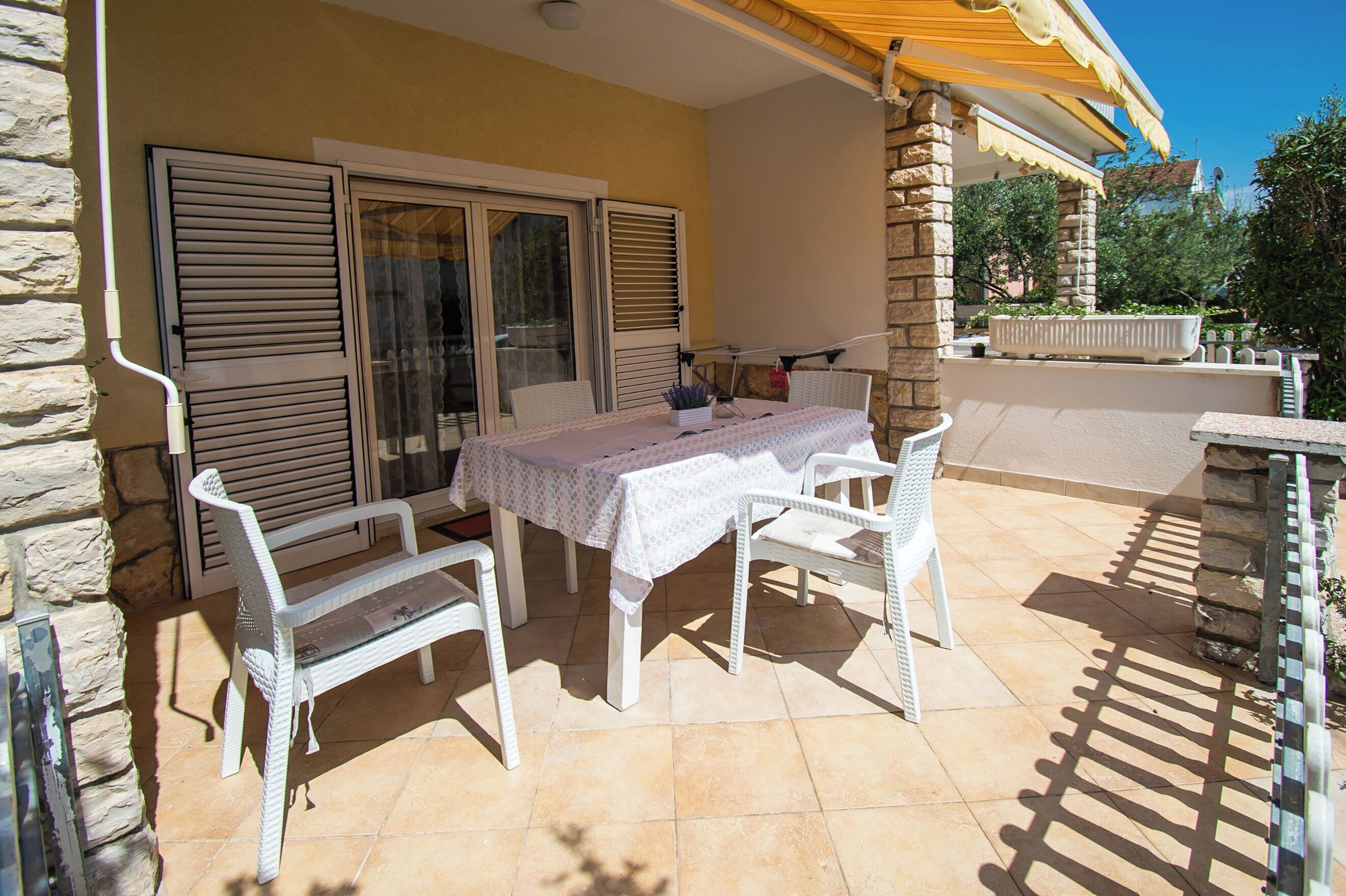 An outdoor patio with a table and chairs, a stone wall, and a covered area with a yellow awning.