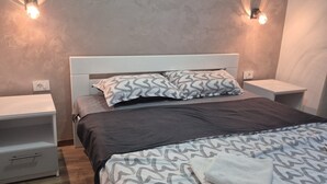 A bedroom with a bed, two bedside tables, a nightstand, a patterned bedspread, and wall-mounted lights. - Apartments Tiho (Vodice)