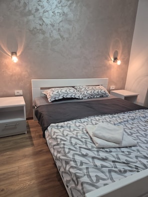 Ein Schlafzimmer mit einem Bett, zwei Nachttischen, einer Nachttischlampe, einer gemusterten Bettdecke und Wandleuchten.